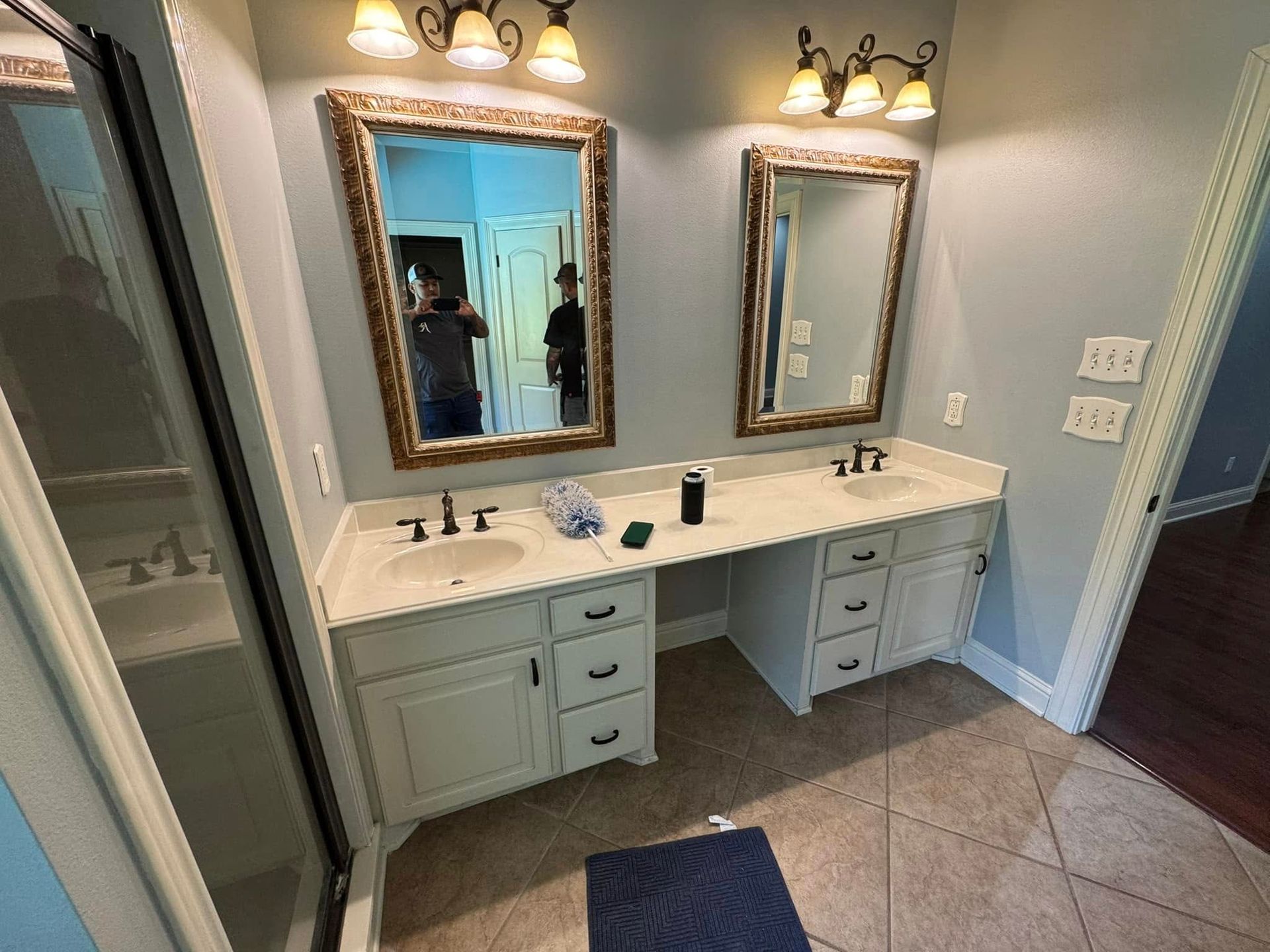 Bathroom vanity with two gold-framed mirrors, white cabinets, and beige tile floor