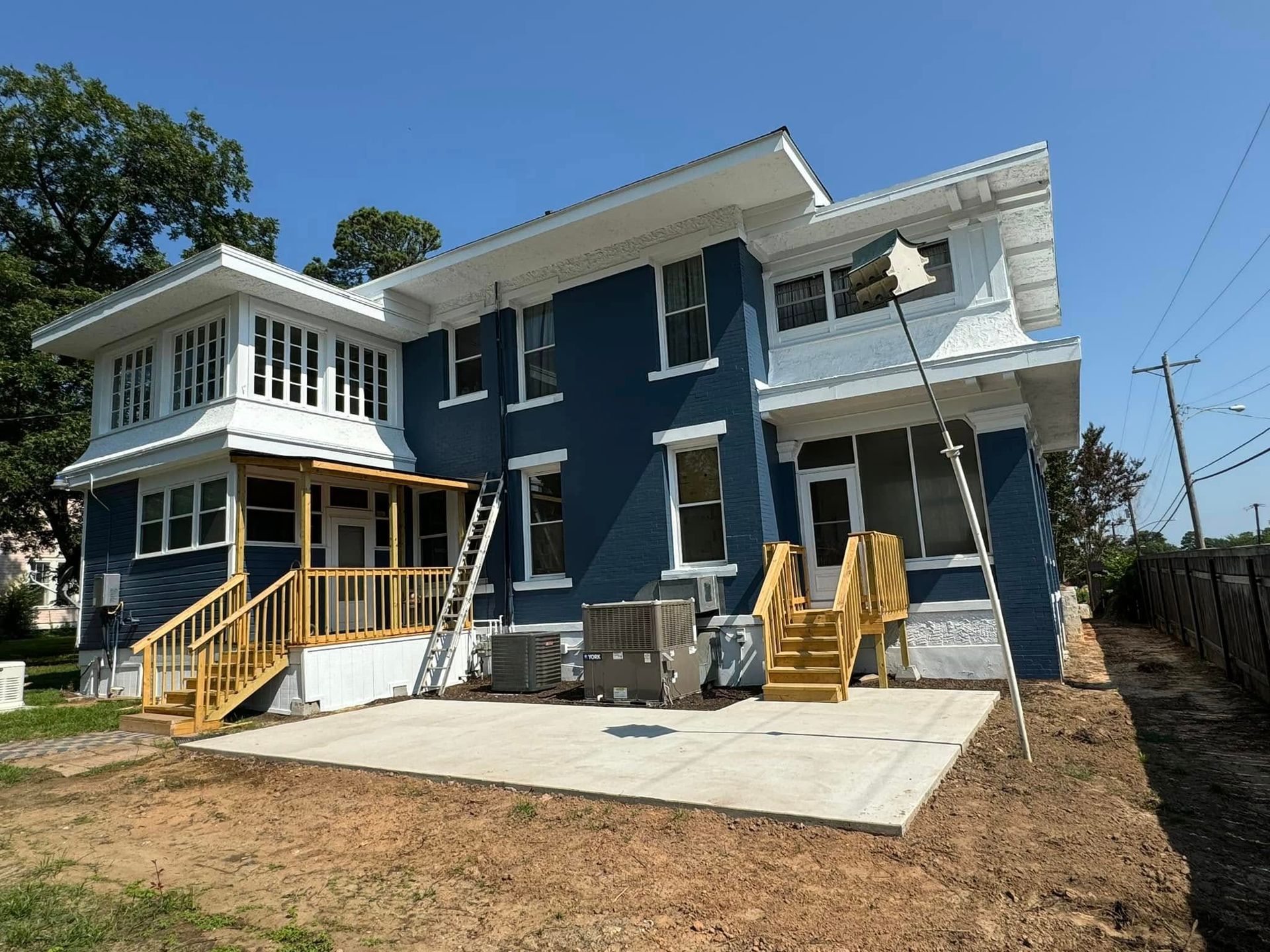 Blue two-story house with white trim and wooden porches under construction on a dirt lot