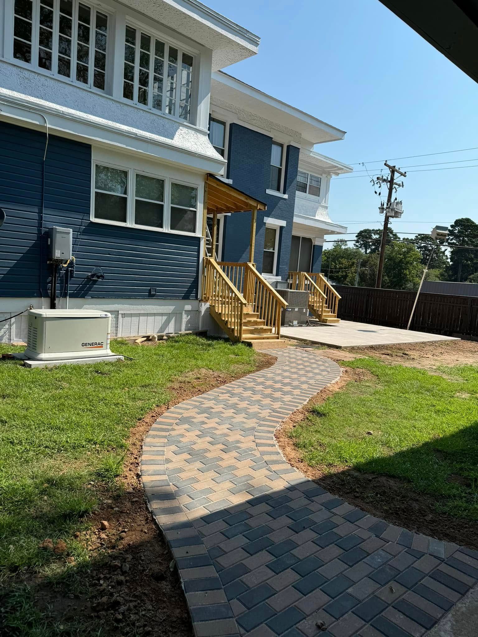 Brick paver walkway leading to a blue townhouse with wooden steps and a small lawn
