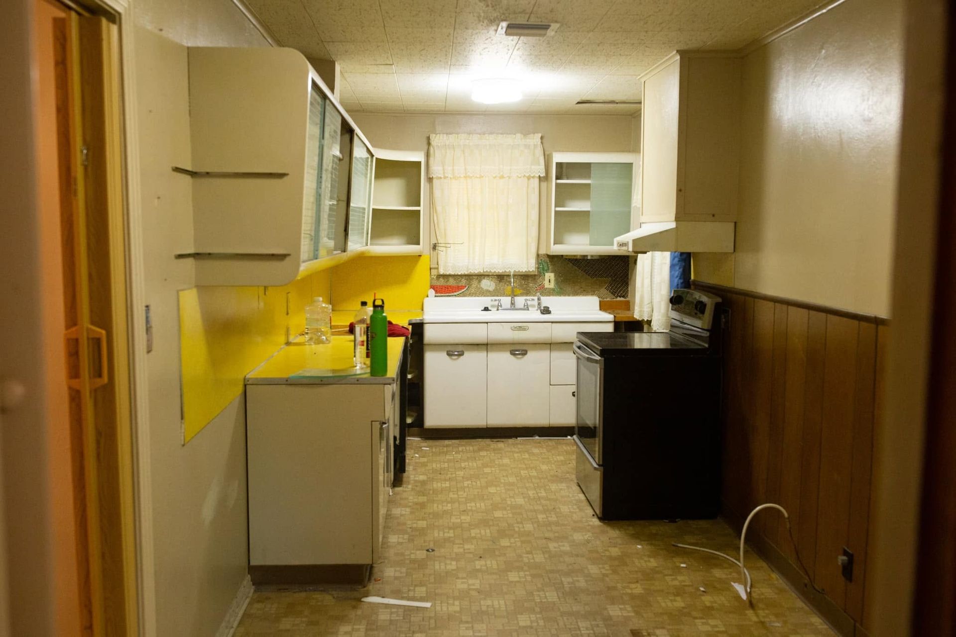 Narrow kitchen with white cabinets, yellow backsplash, and a window above the sink.