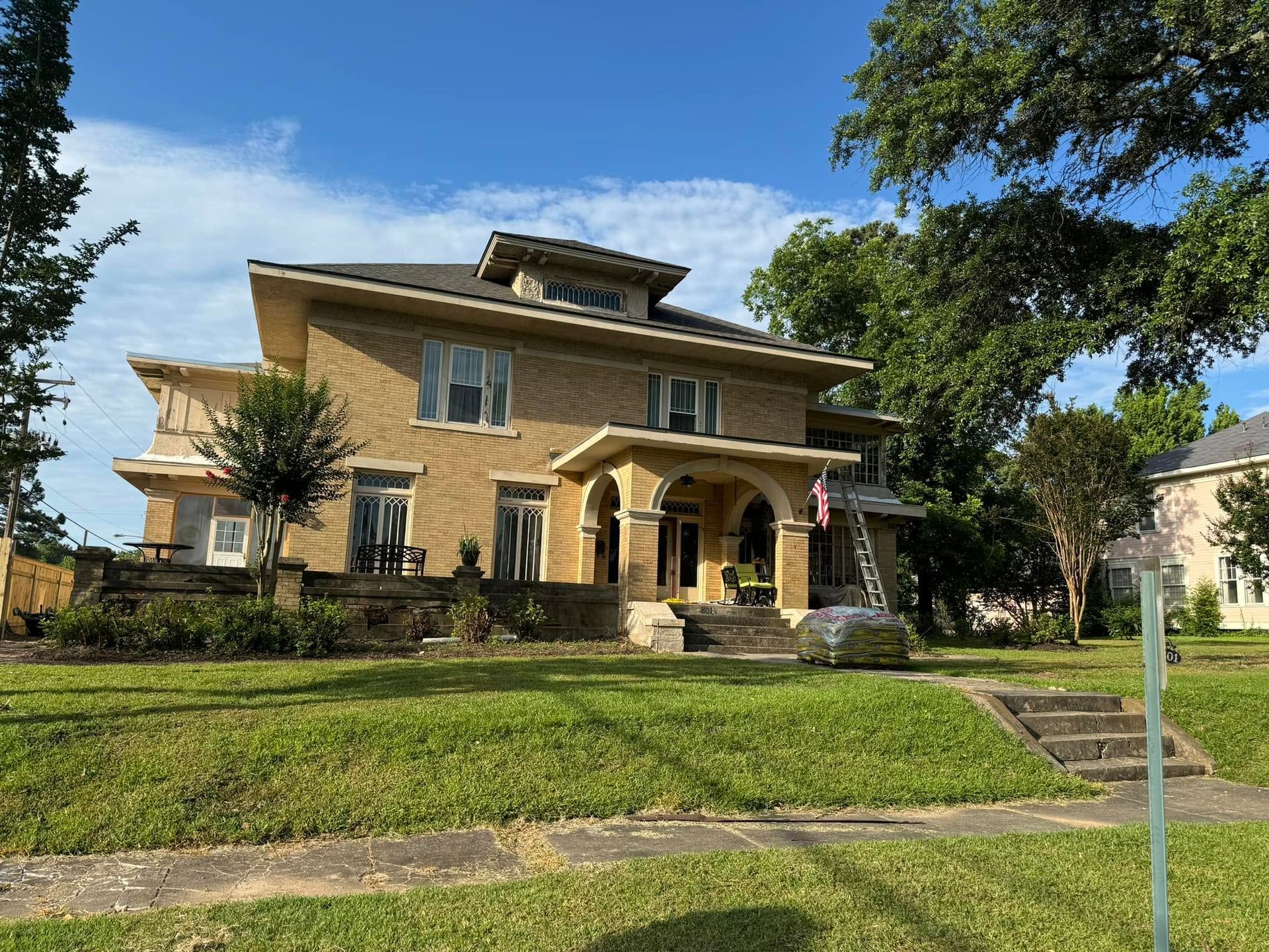 Large tan house with a front porch and lawn under a blue sky