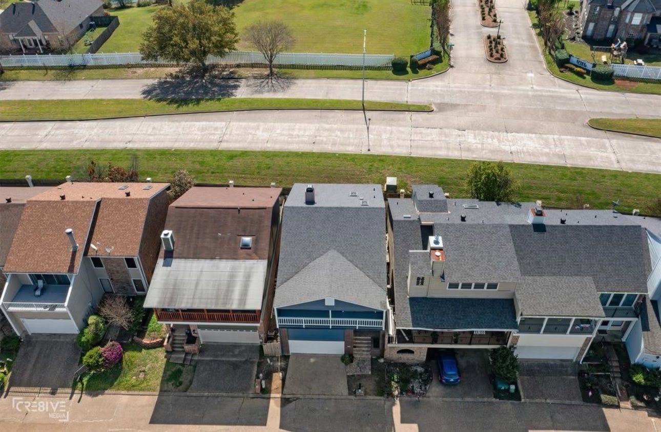 Aerial view of a row of suburban townhouses with driveways and a street behind them.