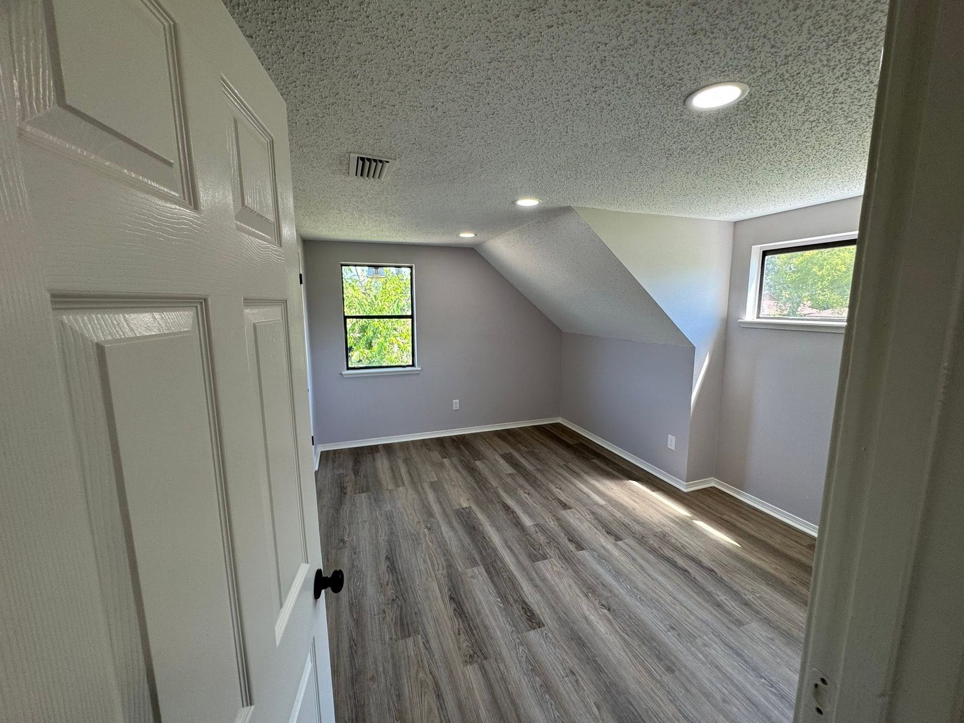 Empty attic-style bedroom with gray walls, sloped ceiling, and wood-look flooring.
