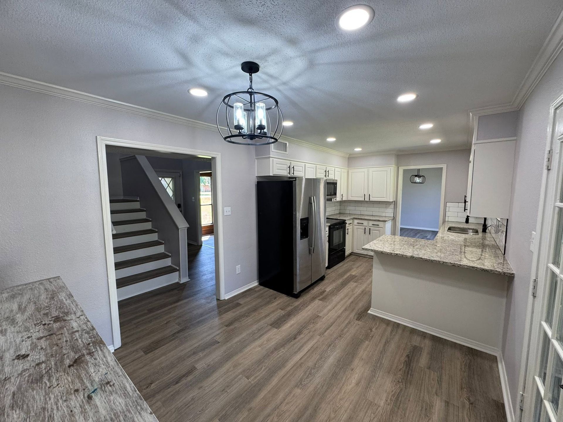 Open-concept kitchen and dining area with gray cabinets, granite island, wood floors, and staircase.