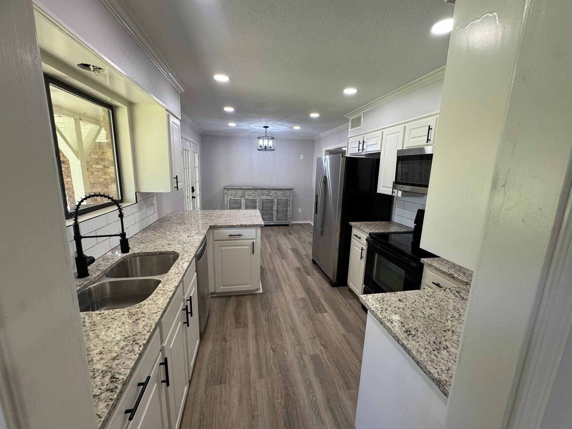 Bright kitchen with white cabinets, granite counters, stainless appliances, and wood-look flooring
