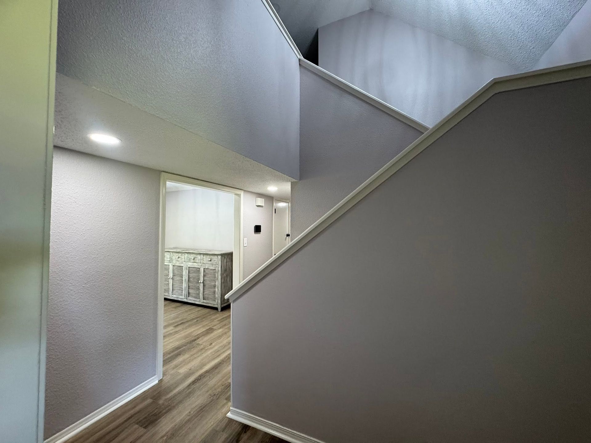 Staircase and hallway in a home with gray walls, wood floors, and bright kitchen visible below.