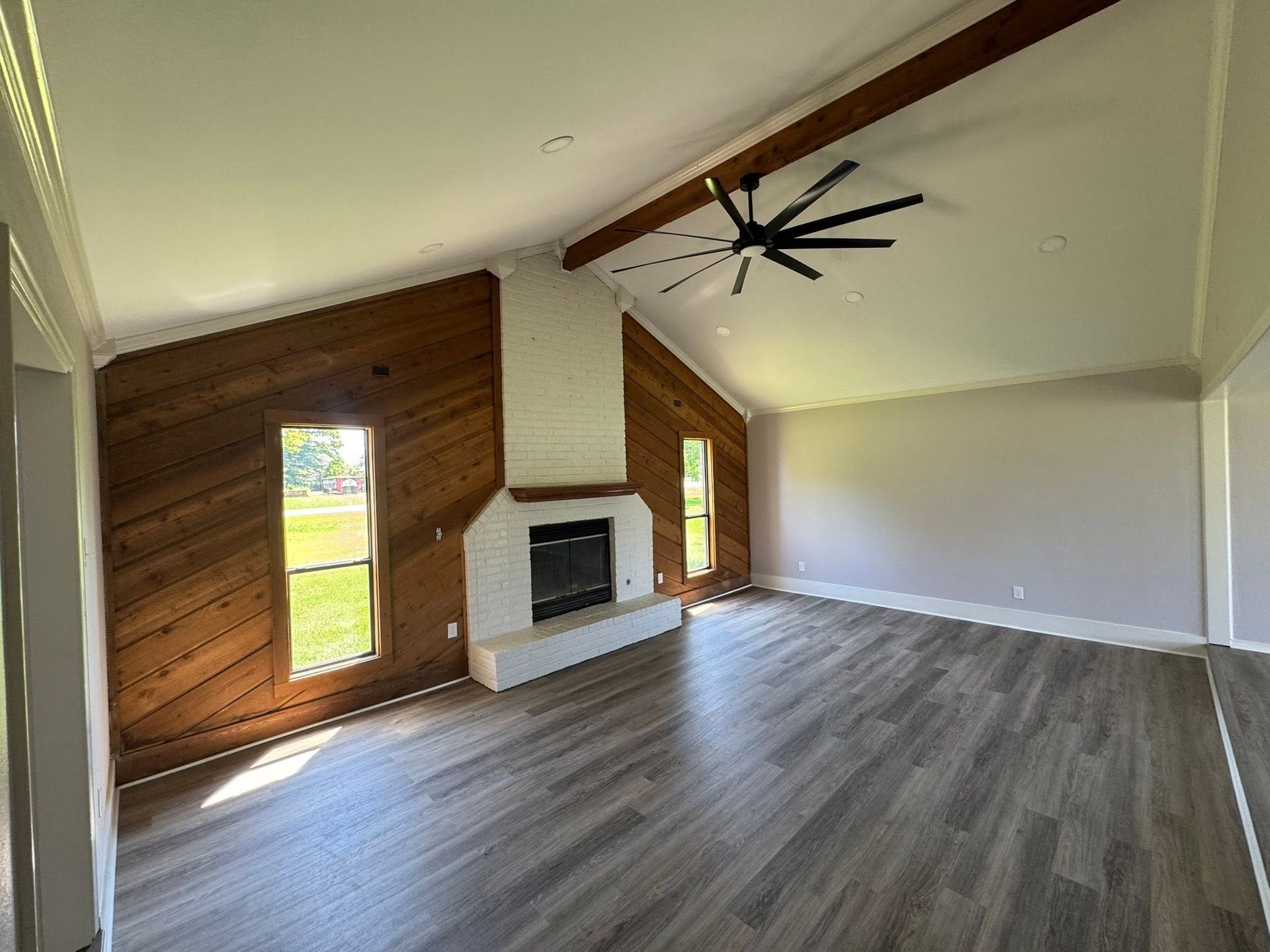 Empty living room with sloped ceiling, fireplace, wood accent wall, and large ceiling fan.