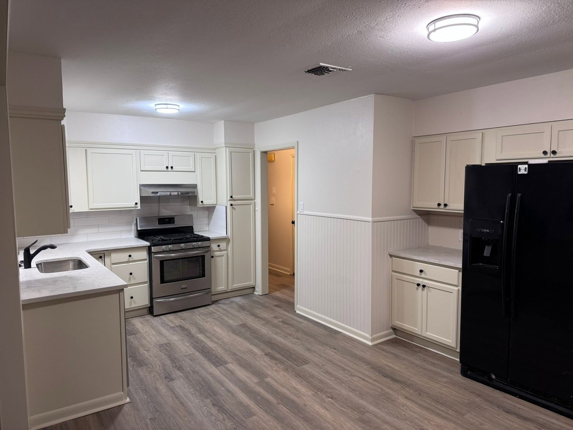 Bright kitchen with white cabinets, gray flooring, stainless stove, and black refrigerator.