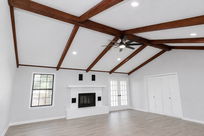 Bright living room with vaulted wood beams, white walls, fireplace, windows, and light wood floors