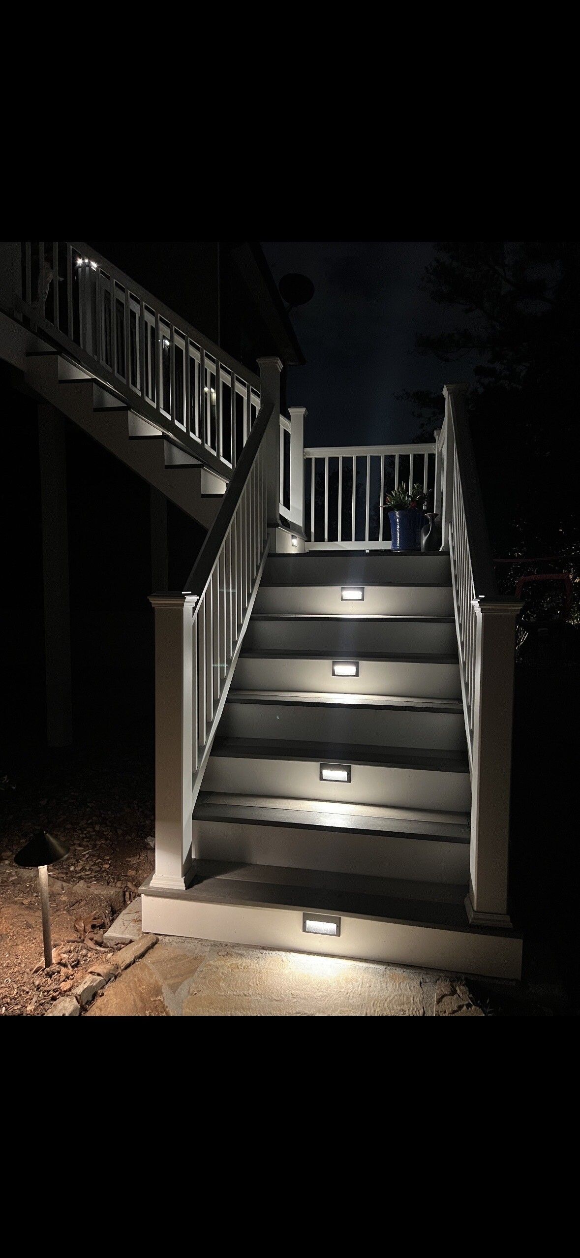 Dimly lit outdoor wooden staircase with railing at night, illuminated by a spotlight.