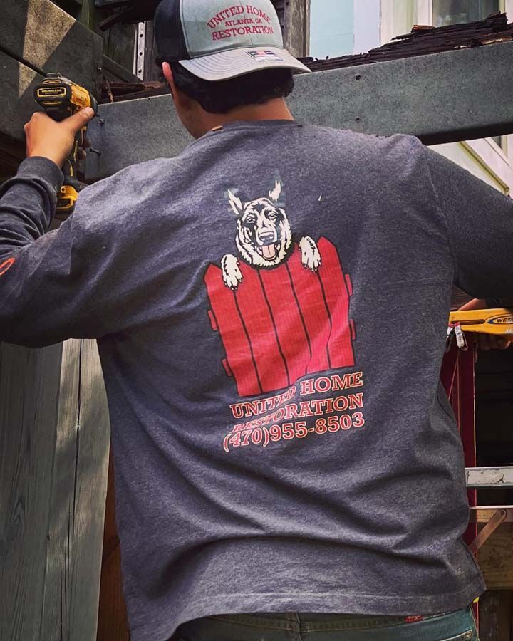 Man wearing a gray shirt with a red graphic on the back, using a drill at a construction site