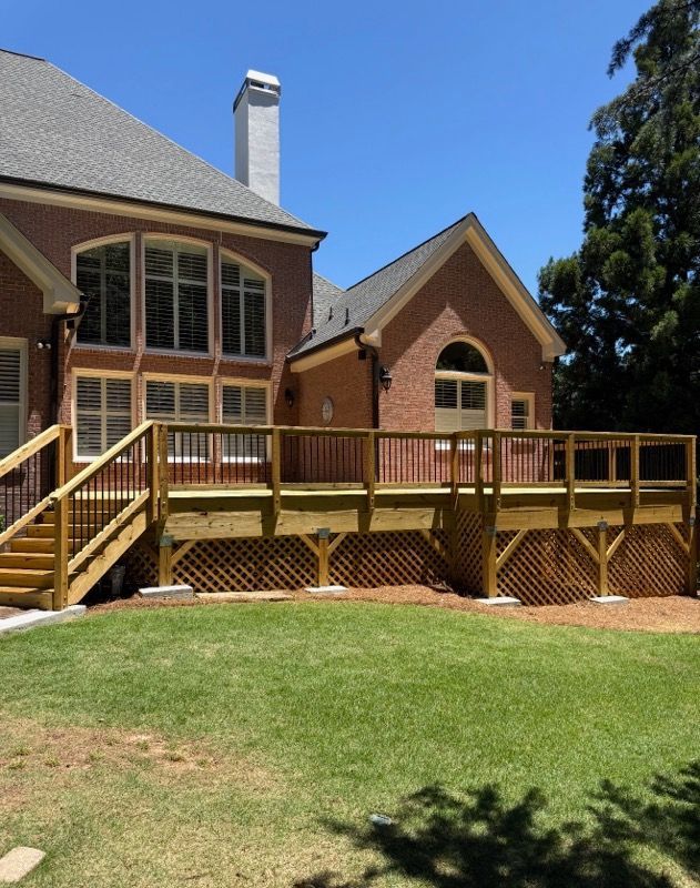 Brick house with a raised wooden deck, stairs, and a green lawn under a blue sky