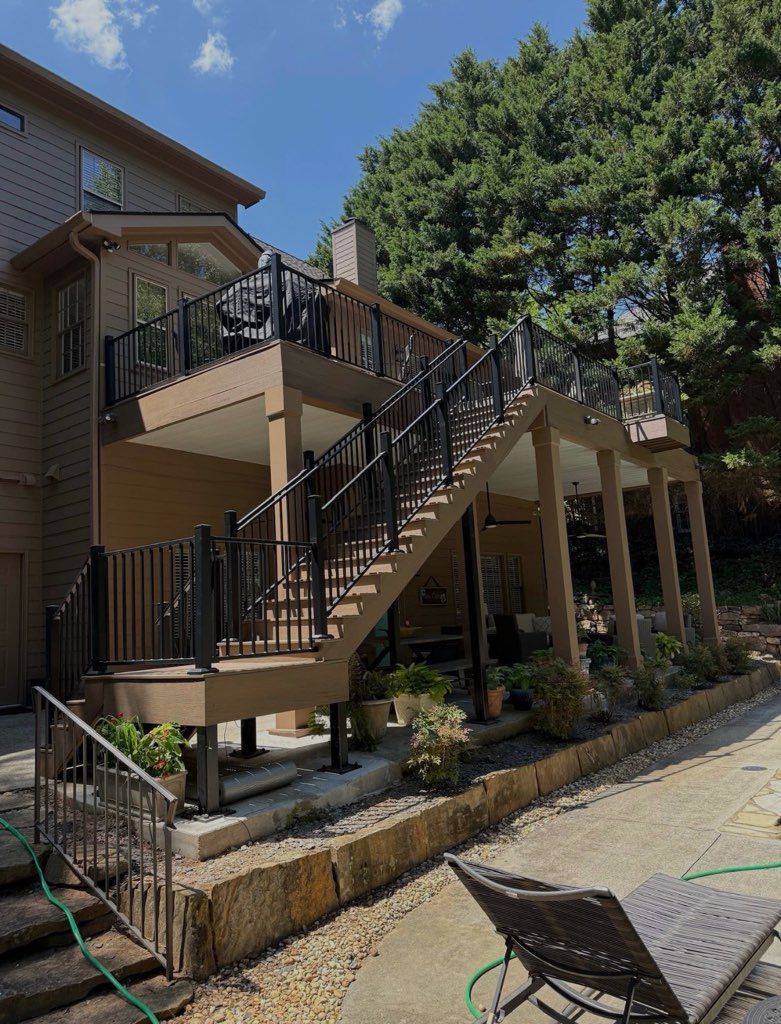 Outdoor staircase and deck attached to a house, with black railings and a stone retaining wall.