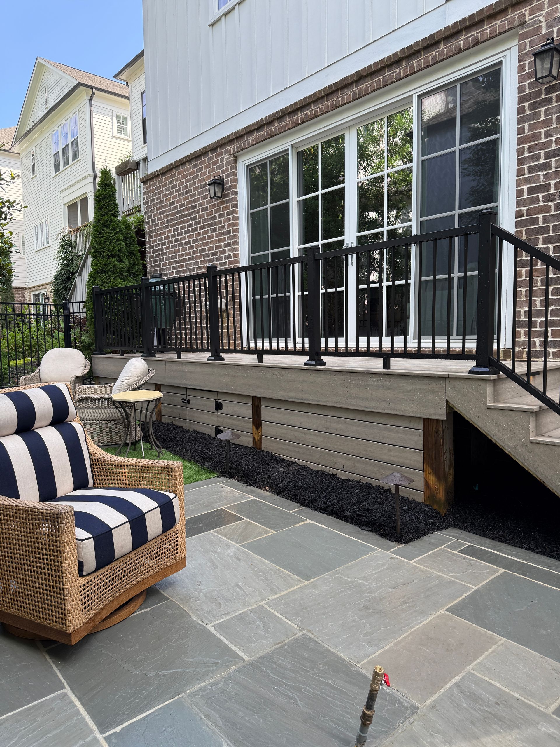 Patio with striped lounge chair, raised deck, black railing, and large glass doors beside a house