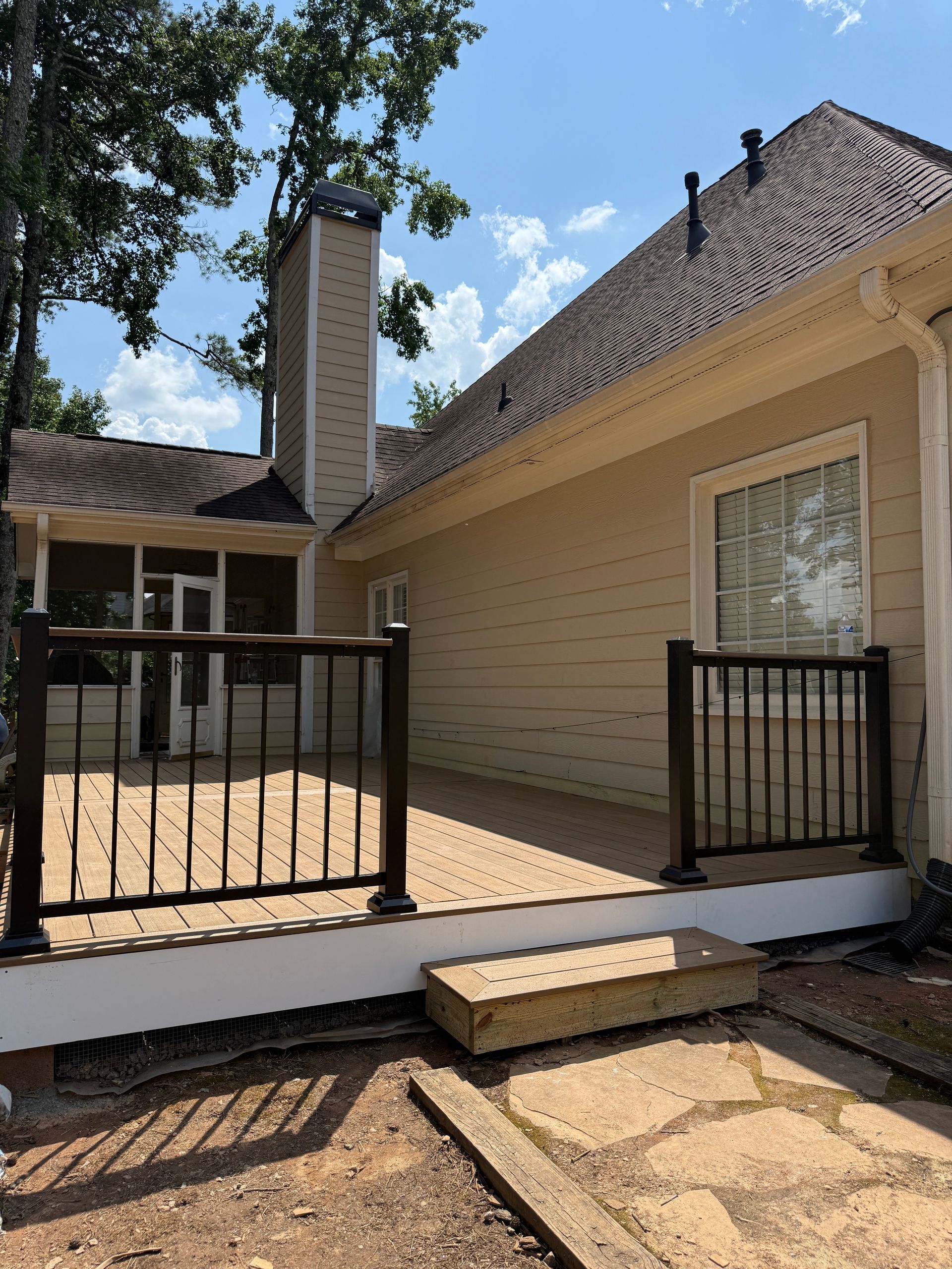 Back patio with black railings, beige house exterior, chimney, and stone walkway under a sunny sky