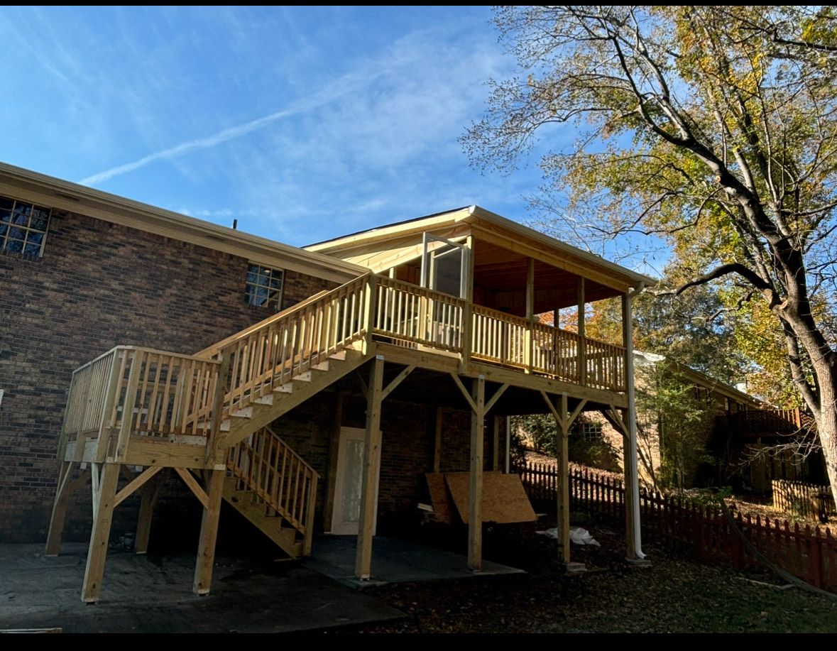 Wooden raised deck with stairs attached to a brick house beside a large tree in a yard