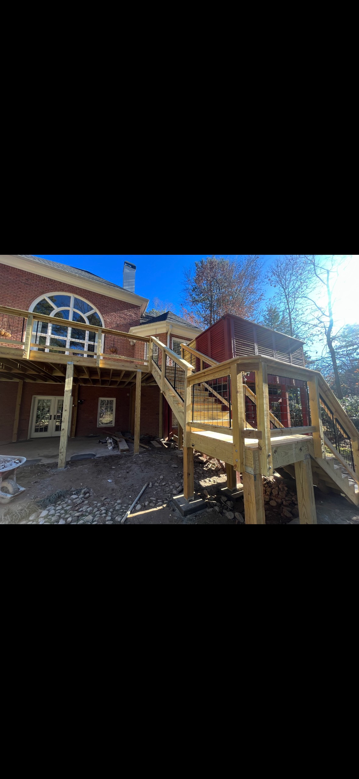 Wooden cabin porch with stairs, railing, and large windows in a wooded setting