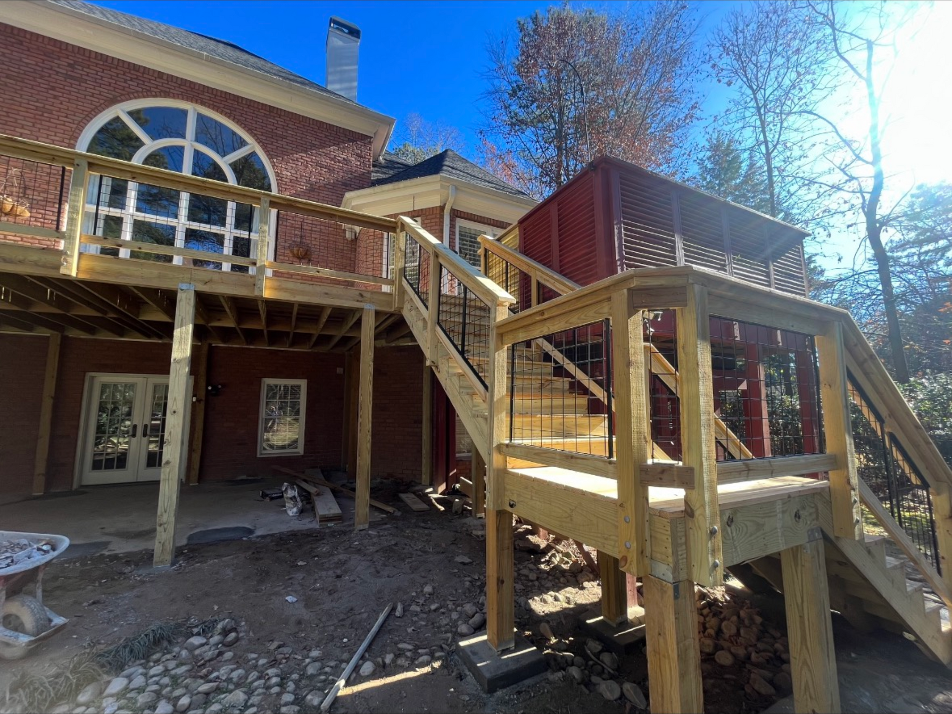Wooden stairs and deck leading to a brick house with an arched window in a wooded yard