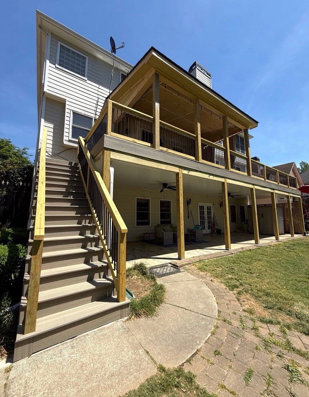 Two-story house with exterior stairs, yellow porch, and a sloped grassy yard under a blue sky