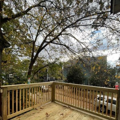Wooden deck with railing overlooking trees and a residential street on a cloudy day