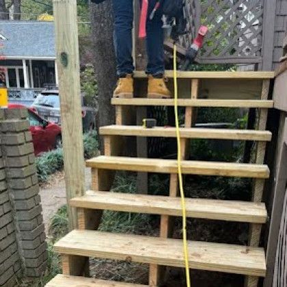 Wooden outdoor stairs under construction with a person standing on the top step holding a yellow measuring tape.
