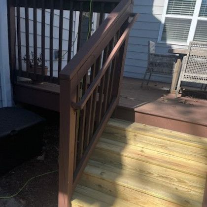 Wooden deck stairs with brown railings leading to a sunlit porch and patio area