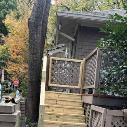 Wooden staircase leading to a gray house porch, with lattice railings and autumn trees nearby