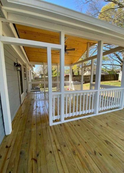 Covered wooden porch with white railings and a sloped roof, overlooking a yard.