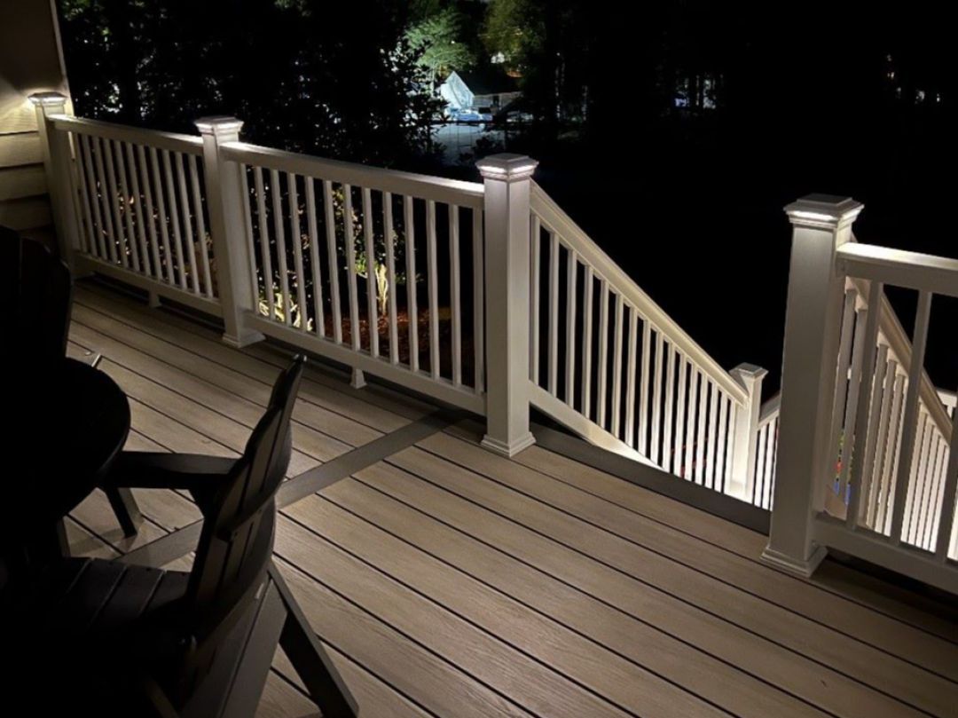 Dimly lit wooden deck with white railings and stairs at night, with chairs in the foreground