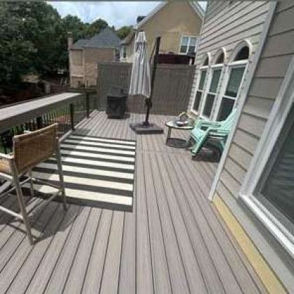 Back patio deck with striped rug, outdoor chairs, closed umbrella, and house siding.