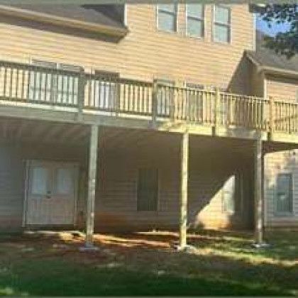 Apartment building with tan siding, elevated balcony, and shaded ground-level patio area
