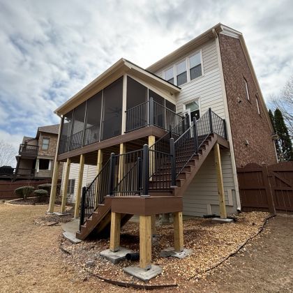 Raised backyard deck with stairs and screened porch attached to a brick two-story house