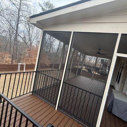 Screened porch with black railings, brown deck flooring, and a wooded view outside
