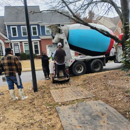 Cement truck pouring gray concrete into a wheelbarrow on a suburban street with workers nearby