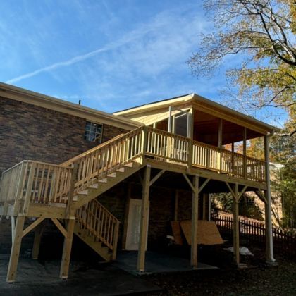 Elevated wooden house deck with stairs and railing under a blue sky