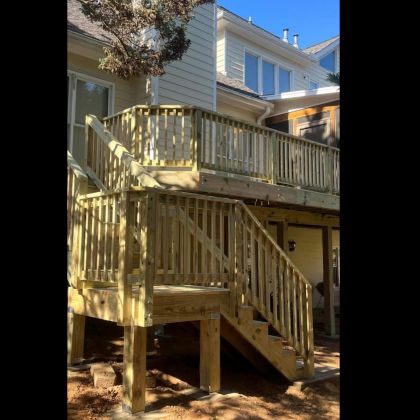 Wooden backyard deck with stairs and railing attached to a house in sunlight