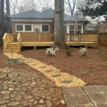 Backyard deck with wooden railing, stone path, and large tree in front of a house.