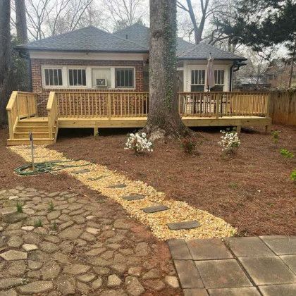 Small house with a wooden deck and stairs, stone and gravel walkway, and leafless trees in front yard