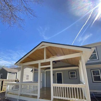 House porch with white railings and a wooden roof under a bright blue sky
