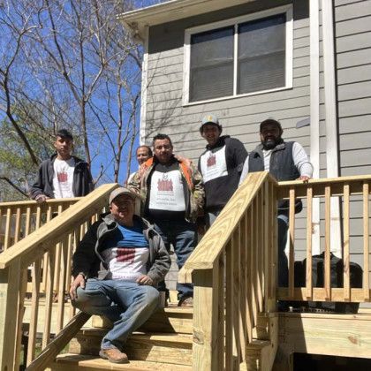 Five people posing on wooden porch steps outside a house on a sunny day