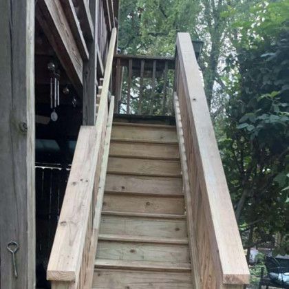 Wooden outdoor stairs leading to a deck, surrounded by trees and greenery.