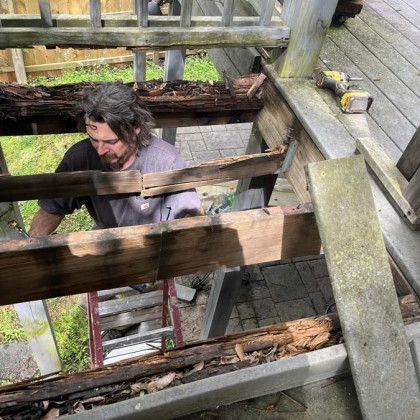 Man working inside a wooden scaffold or shaft, viewed from above, with mossy wood beams around him
