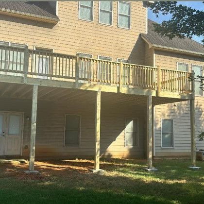 Back deck on a beige apartment building with wooden railings and support posts, sunlit yard below