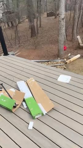 Wooden deck with scattered cardboard and foam debris beside a wooded yard and a red stake marker