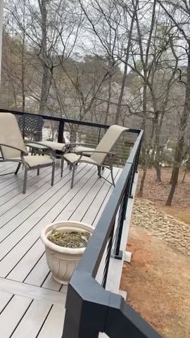 Outdoor deck with beige chairs, a small table, and a potted plant overlooking leafless trees.