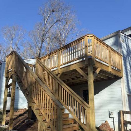 Wooden outdoor staircase and elevated deck attached to a light blue house under a clear blue sky