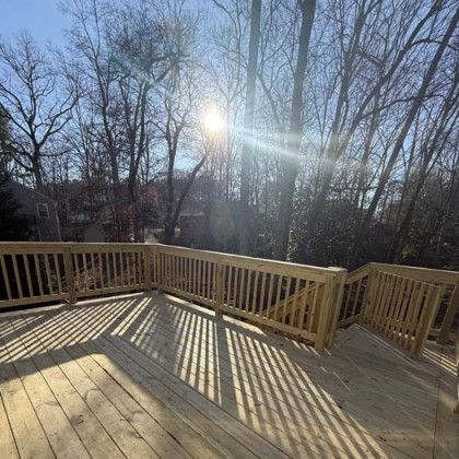 Wooden deck with railing overlooking leafless trees in bright winter sunlight