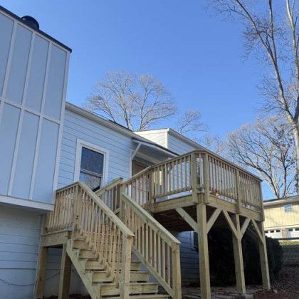 Wooden deck and stairs on the side of a light blue house under a clear blue sky