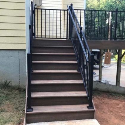 Outdoor wooden staircase with black railings leading up to a deck beside a house