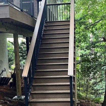 Wooden outdoor staircase leading to a raised deck amid trees and greenery